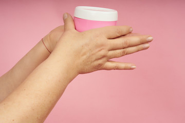 Senior woman hands applying cream on hands on coral background