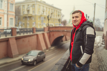 Fototapeta premium Stylish handsome young man. A young man in a black jacket walks through the old town. Stylishly dressed young man on the street. The guy in the center of the city. Travel to a European city.