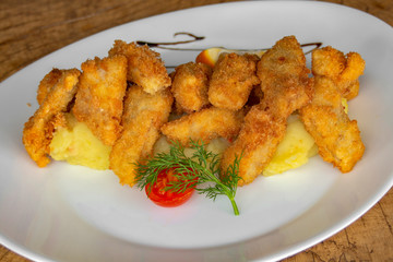 Breaded white fish. Garnished with mashed potatoes, cherry tomatoes, stalks of dill and slice of lemon.