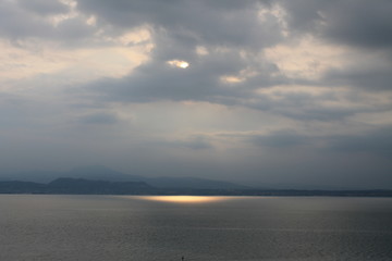 Naklejka na ściany i meble The sun breaking through the clouds over lake Garda Italy