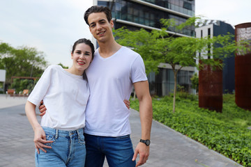 Obraz premium Front view of beautiful young couple hugging, looking at camera and smiling while standing outdoors