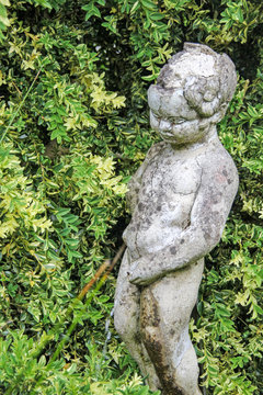 Old statue of a boy standing urine in a garden, which is sunken in oblivion.