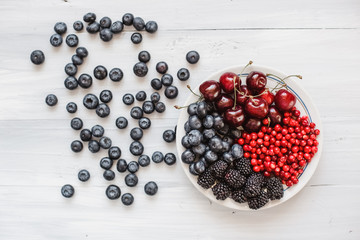 Berries platter with fresh organic red cowberry, blueberry, cherries and blackberry wooden table, top view.