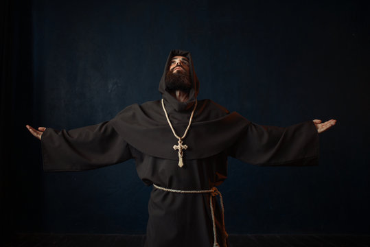 Monk in black robe with hood kneeling and praying