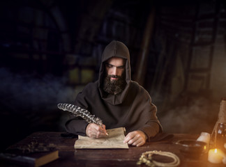 Medieval monk in robe writes with a goose feather