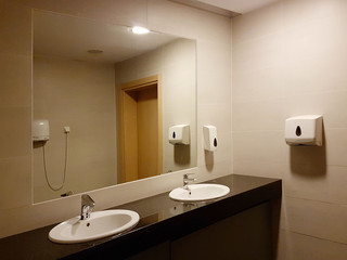 Bathroom interior in black and white. Round ceramic washbasins. Mirrors, plastic soap dish and chrome faucets for washing hands after a toilet. Design with dark facing tiles