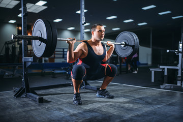 Fototapeta na wymiar Powerlifter doing squats with barbell in gym