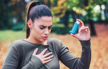 Young woman treating asthma with inhaler - obrazy, fototapety, plakaty