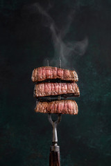 Slices of beef steak with steam on vintage fork on dark background - 256072633