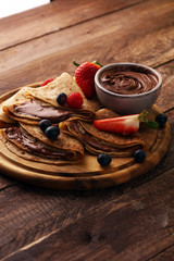 Delicious Tasty Homemade crepes with chocolate or pancakes with raspberries and blueberries on rustic wood