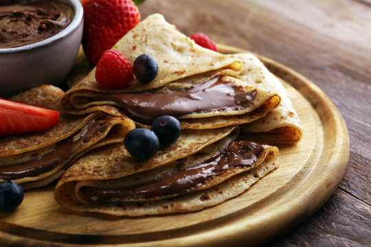 Delicious Tasty Homemade crepes with chocolate or pancakes with raspberries and blueberries on rustic wood