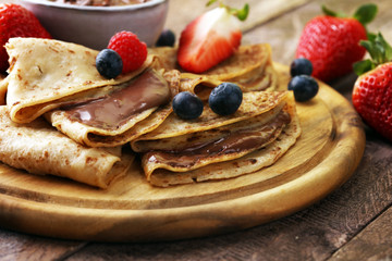 Delicious Tasty Homemade crepes with chocolate or pancakes with raspberries and blueberries on rustic wood