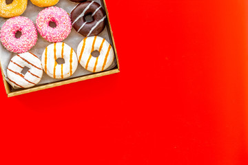 Glazed decorated donuts in box on red background flat lay mock up