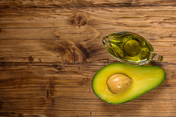 Avocado oil in a glass bowl and fresh organic avocado on old wooden background.Healthy eating,diet,body care concept. Space for text. Top view.