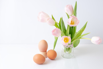 three colored eggs lie next to a bouquet of pink tulips in a glass jar. The concept of Easter