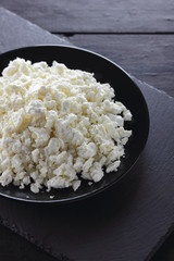 Cottage cheese on black slate board. Cheese on black plate. Soft cheese for diet on black boards. Healthy dairy product for breakfast. Concept