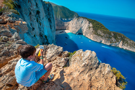 A boy on the edge of the cliff in the background of Shipwreck Bay, Zakynthos Island, Greece