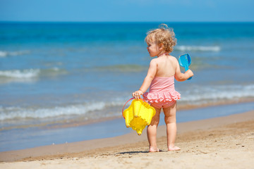 Child playing on tropical beach. Little girl digging sand at sea shore. Kids play with sand toys. Travel with young children