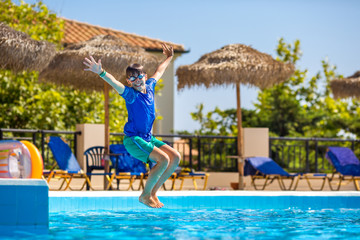 Little cheerful boy jumping to the pool and making water splash, enjoying time in the refreshing water