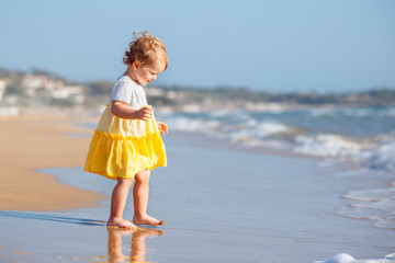 Cute curly baby girlwearing a yellow dress playing on a beautiful tropical beach