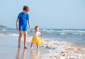 Kids playing on tropical beach. Big brother together with his little sister at sea shore at sunset....