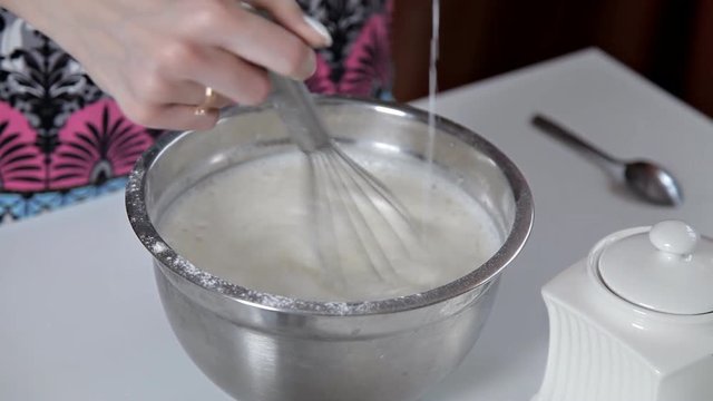 A woman pours milk from a cup into a bowl with dough. The girl prepares pancakes, cookies, dough