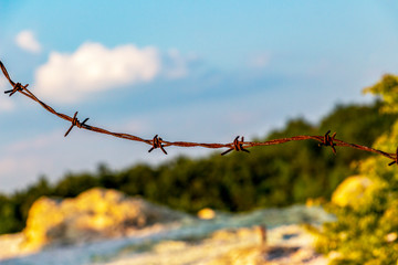 Close-up of rusty barbed wire on a natural blurred background, fence of the Stone Mushrooms near Beli Plast village, Bulgaria - obrazy, fototapety, plakaty