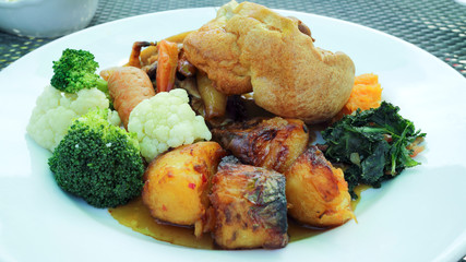Vegetarian meal of Yorkshire pudding, roast potatoes, chunks of carrots, broccoli, cauliflower, spinach, served on a white plate.