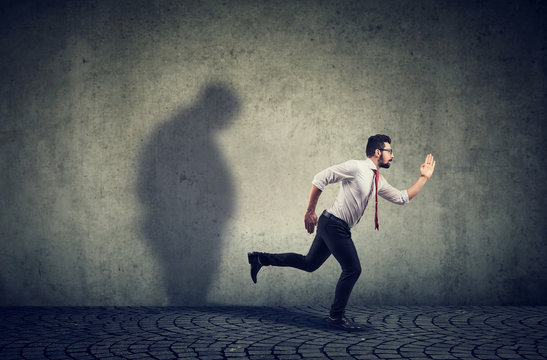 Man running away from his sad gloomy fat shadow on the wall.