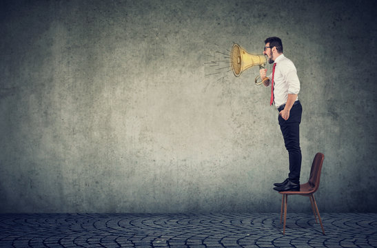 business man standing on a chair and screaming into a megaphone