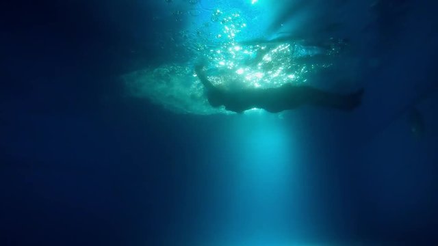 Woman dives under water among the rays of light and air bubbles.