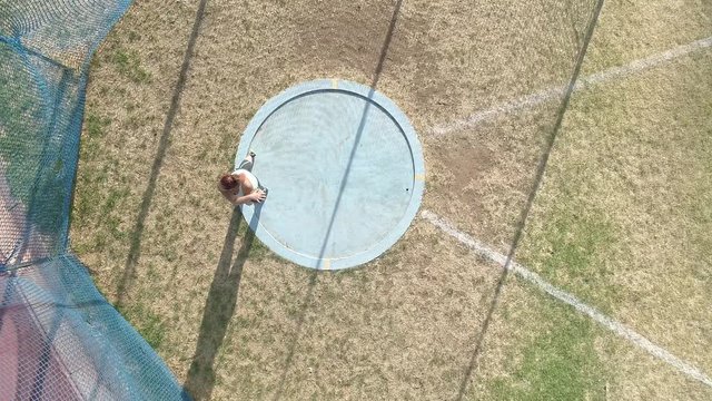 Aerial footage of a female discus athlete doing practice throws in a discus ring on a track and field stadium