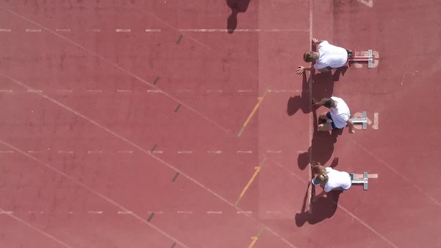 Aerial view over a three sprinter athletes sprinting away from the start line