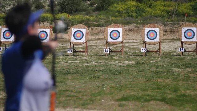 Archery, over the shoulder view of a blurred archer practicing shooting at outdoor targets
