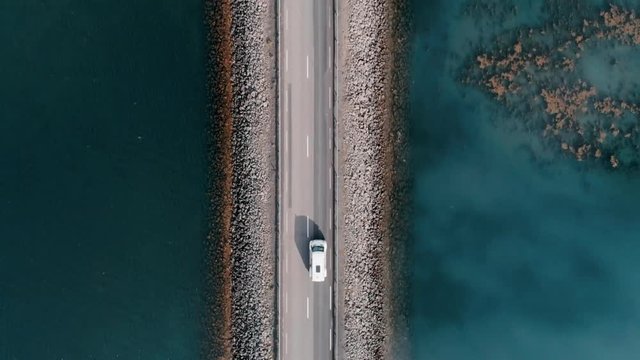 Straight down aerial shot on bridge or rised up road connecting two sides of lake or bay through beautiful blue water. Concept logistics and transportation. Camper van or caravan on travel roadtrip