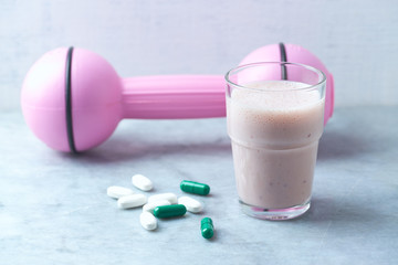 Glass of Protein Shake with milk and raspberries. BCAA amino acids, L - Carnitine capsules and pink dumbbell in background. Sport nutrition. Stone / Wooden background. Copy space. 