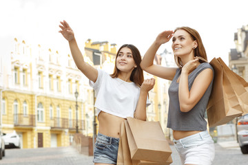 Look at this! Beautiful brunette smiling and pointing at the shop to her friend, both carrying...