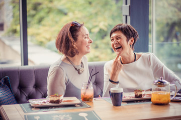 Laughing aged women enjoying meeting in cafe