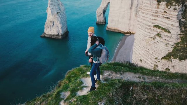 Drone spins close around young happy tourist couple standing together on top of famous Normandy sunset white coast cliff