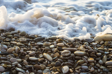 pebble stones on the sea beach, the rolling waves of the sea with foam