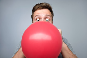Young european man blowing up a red balloon