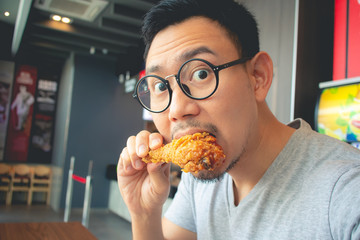 Funny face of man eat fried chicken in the franchise cafe.