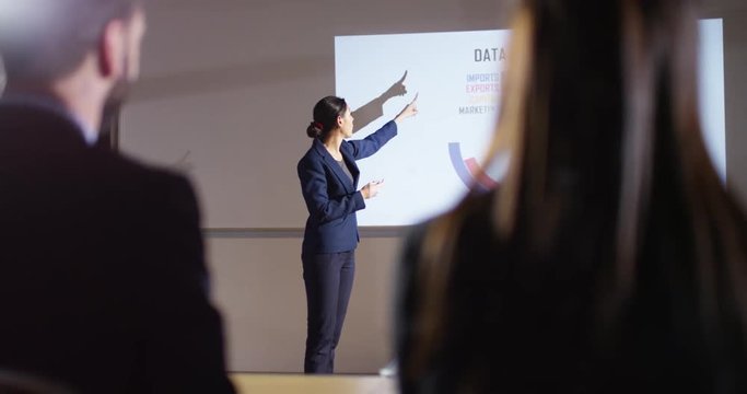 4K Hispanic businesswoman giving a presentation, showing animated graphs on screen. Slow motion.