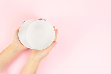 Woman holding silicone implants for breast augmentation on color background, top view with space for text. Cosmetic surgery