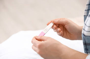 Young woman with pregnancy test at home, closeup. Space for text