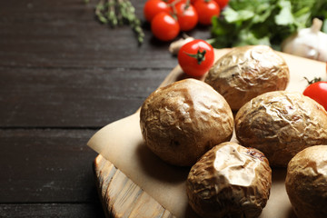 Board with tasty baked jacket potatoes on wooden table, closeup. Space for text