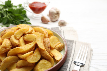 Plate with tasty baked potato wedges on wooden table, closeup. Space for text