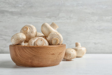 Bowl with fresh champignon mushrooms on wooden table, space for text