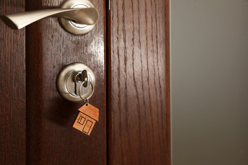 Key with house-shaped trinket in door lock, closeup view