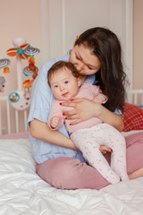 Portrait of beautiful mixed race Asian mother kissing touching embracing her cute adorable newborn infant baby. Early development and health care lifestyle concept. Family in bedroom